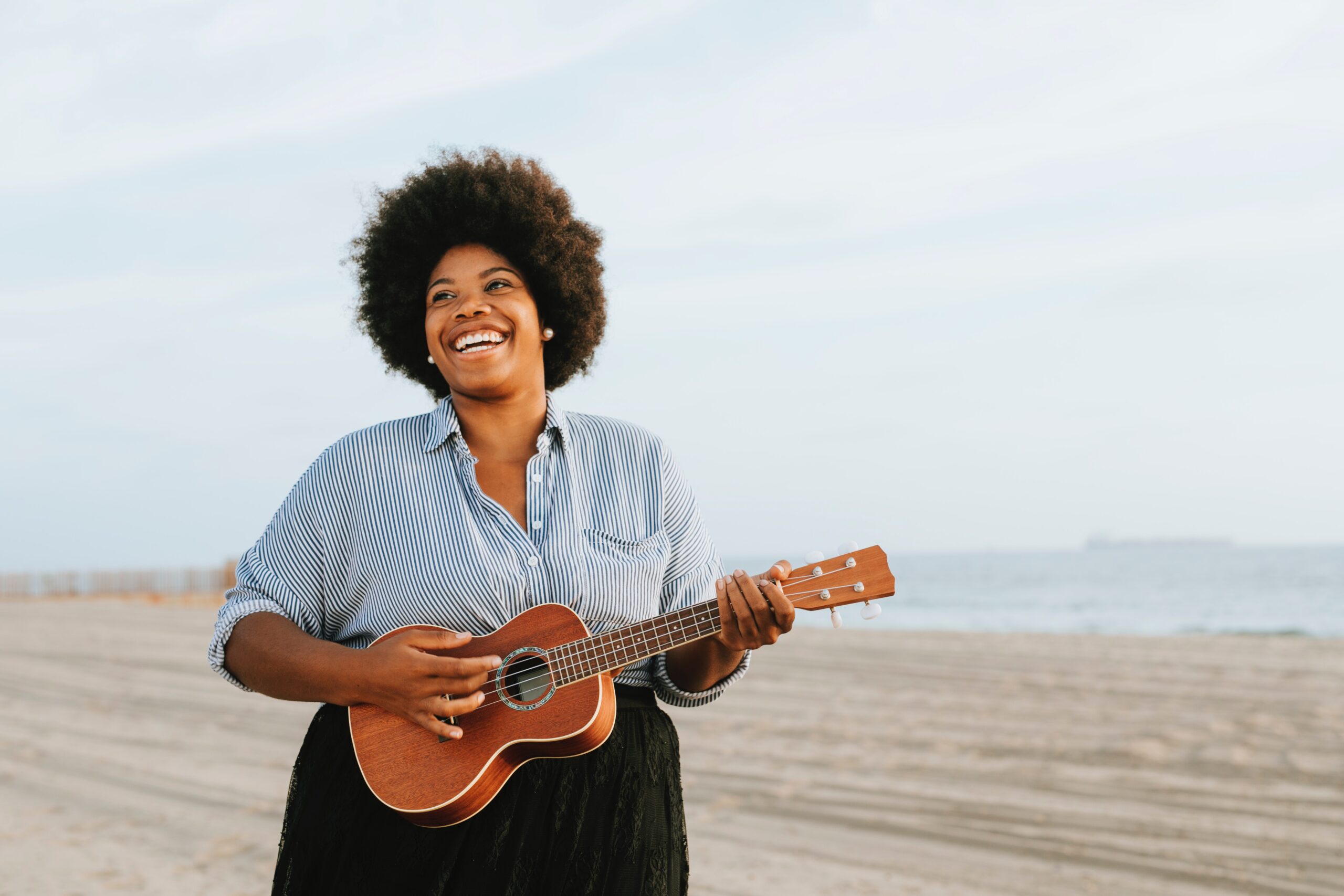 Lady playing guitar on a beach. Representing guitar and strings lessons at SFE Music School